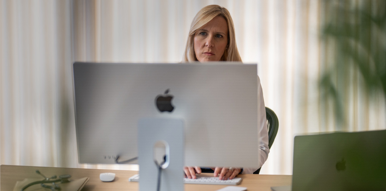 مزودة خدمة تنظر إلى شاشة iMac من خلف مكتبها.