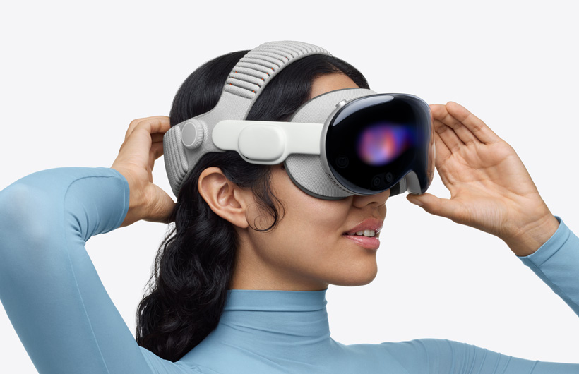 Une personne portant un Apple Vision Pro, avec bandeau tissé à sangle double, la sangle supérieure passe sur le dessus de la tête, une main est placée sur la sangle inférieure à l’arrière de la tête, l’autre main est placée sur la monture en alliage d’aluminium