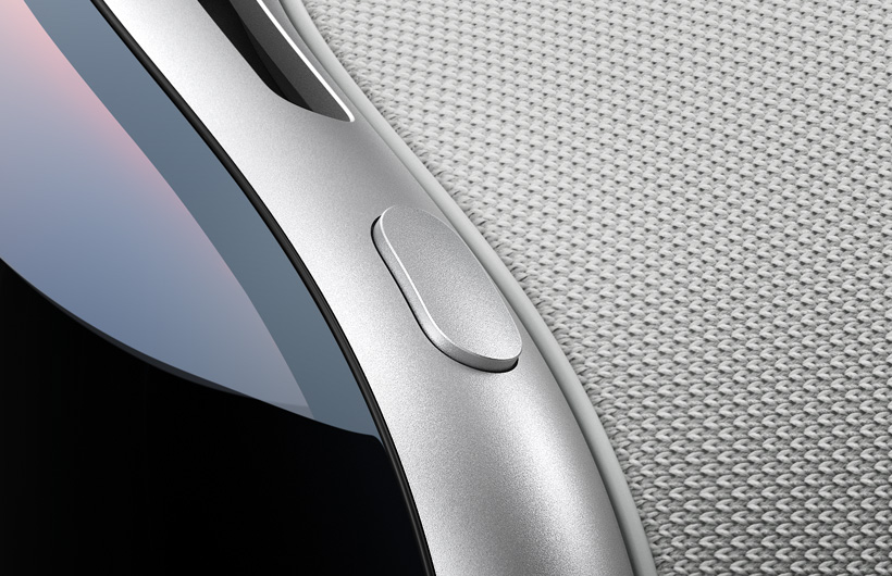 Gros plan montrant le coin arrondi supérieur gauche d’un Apple Vision Pro, le bouton supérieur a le même fini en aluminium que la monture d’Apple Vision Pro, le verre avant incurvé et une partie de la fente d’aération supérieure sont aussi visibles