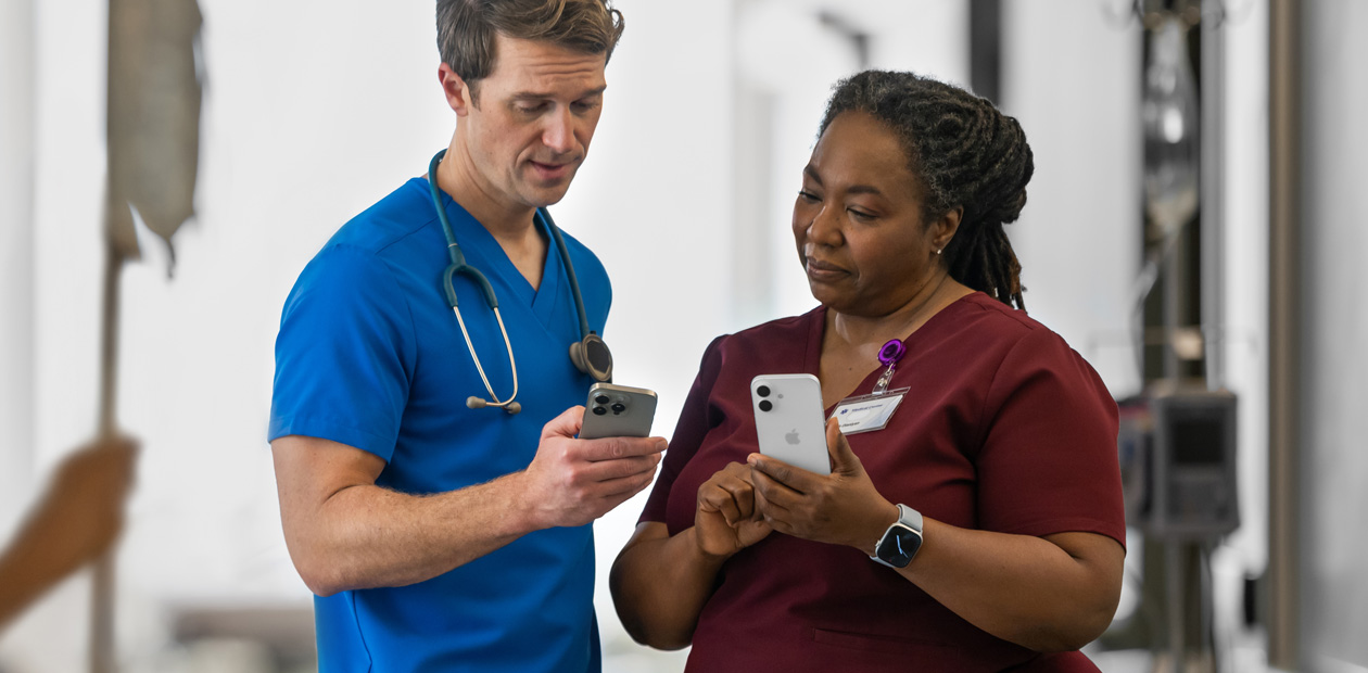 Un médecin portant un uniforme bleu montre quelque chose sur son iPhone à une médecin portant un uniforme rouge, qui tient aussi un iPhone.