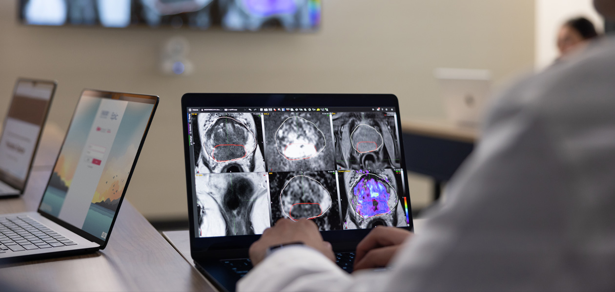 Pessoa revisando exames médicos em um MacBook. Dois outros aparelhos MacBook estão abertos no fundo.