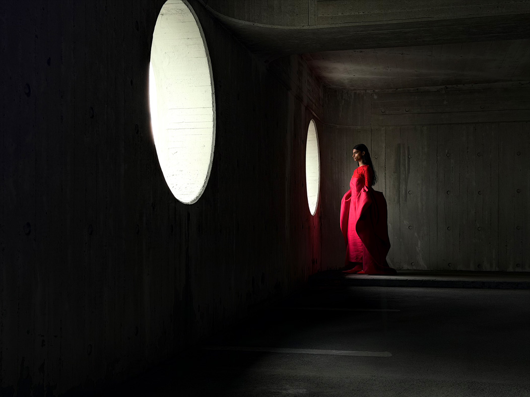 Une femme vêtue d’une longue robe rouge se fait photographier dans une pièce vide. L’app Appareil photo change de distance focale pour illustrer les capacités du système caméra pro, mettant en valeur : 48 mm